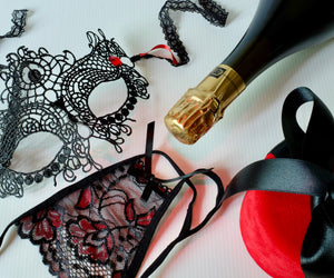 Perizoma nero, maschera da ballo, bottiglia di champagne e astuccio rosso.